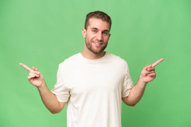 Yeşil krom arka planda izole edilmiş yakışıklı beyaz adam parmak uçlarını gösteriyor ve mutlu.