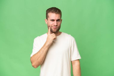 Genç yakışıklı beyaz adam yeşil krom arka planda izole edilmiş ve düşünüyor.