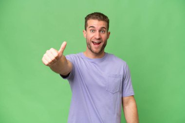Genç beyaz adam yeşil krom arka planda izole edilmiş. Başparmakları havada. Çünkü iyi bir şey oldu.