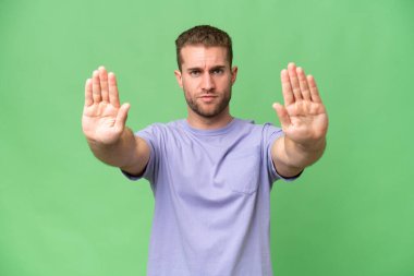 Yeşil krom arka planda izole edilmiş yakışıklı beyaz adam dur hareketi yapıyor ve hayal kırıklığına uğruyor.