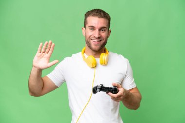 Genç yakışıklı bir adam, yeşil krom arka planda izole edilmiş bir video oyunu kontrolörüyle oynuyor. Mutlu bir ifadeyle selamlıyor.