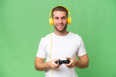 Yeşil krom arka planda izole edilmiş bir video oyunu kontrolörüyle oynayan genç yakışıklı adam.