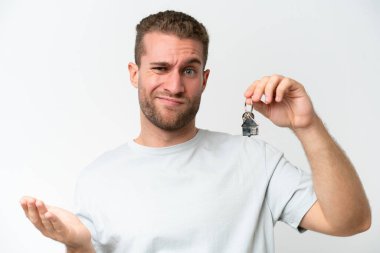 Young caucasian man holding home keys isolated on white background saluting with hand with happy expression