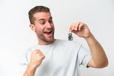 Young caucasian man holding home keys isolated on white background and pointing it