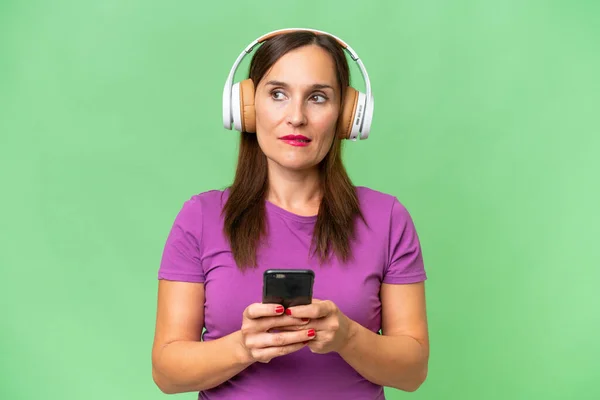 モバイルと思考で音楽を聞いて隔離された背景の上に中年の白人女性 — ストック写真