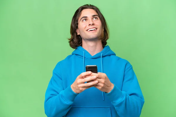 若いですハンサムな男隔離された上で緑のクロマ背景使用して携帯電話と検索アップ — ストック写真