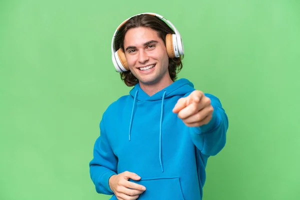 Молодий Красивий Чоловік Ізольований Зеленому Хромовому Фоні Слухаючи Музику Вказуючи — стокове фото