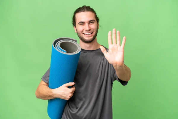 年轻的运动员一边参加瑜伽课 一边拿着垫子盖住孤立的背景 用手指数着五个人 — 图库照片