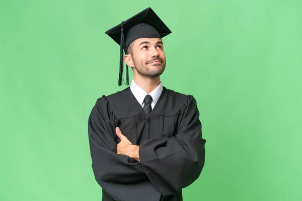 Fiatal Egyetemi Diplomás Férfi Elszigetelt Háttérrel Néz Fel Miközben Mosolyog — Stock Fotó
