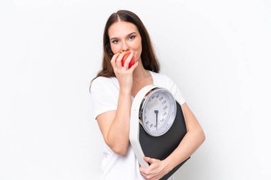 Beyaz arka planda, tartı makinesi ve elmasıyla izole edilmiş genç beyaz bir kadın.