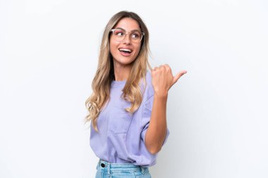 Genç Uruguaylı kadın beyaz arka planda izole edilmiş bir ürün sunmak için kenarı işaret ediyor.