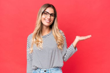 Genç Uruguaylı kadın, kırmızı arka planda izole edilmiş bir şekilde, bir ilan vermek için avucunun içinde hayali bir kopyalama alanı tutuyor.