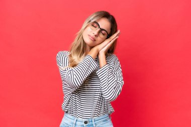 Genç Uruguaylı kadın kırmızı arka planda izole edilmiş bir şekilde uyku jesti yapıyor.