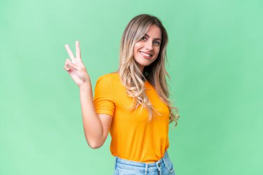 Genç Uruguaylı kadın izole bir arka planda gülümsüyor ve zafer işareti gösteriyor.