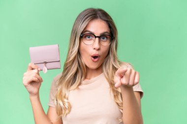 Genç Uruguaylı kadın izole arka planda bir cüzdan tutuyor şaşırmış ve ön tarafı işaret ediyor.