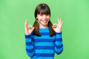 İzole edilmiş arka planda küçük beyaz bir kız iki eliyle tamam işareti gösteriyor.