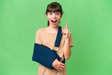 Kırık kollu beyaz bir kız ve izole edilmiş arka planda askı takıyor. Çözümü bulmak için parmağını kaldırıyor.