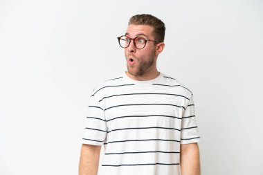 Beyaz arka planda izole edilmiş yakışıklı beyaz adam yan tarafa bakarken sürpriz jest yapıyor.