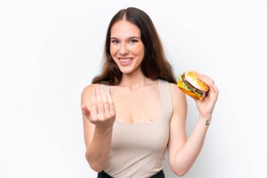 Elinde hamburgerle beyaz arka planda izole edilmiş genç, beyaz bir kadın, bizimle gelmesi için davet ediyor. Gelmene sevindim.