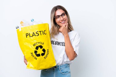 Genç, güzel Uruguaylı bir kadın elinde plastik şişelerle dolu bir çanta ile beyaz arka planda izole edilmiş bir şekilde bir fikir üretiyor.