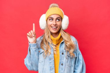 Genç, güzel Uruguaylı kadın, kırmızı arka planda izole edilmiş kış kürkleri giyiyor. Çözümün farkına varmak için parmağını kaldırıyor.