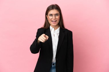 Genç beyaz kadın pembe arka planda izole edilmiş şaşırmış ve ön tarafı işaret ediyor.