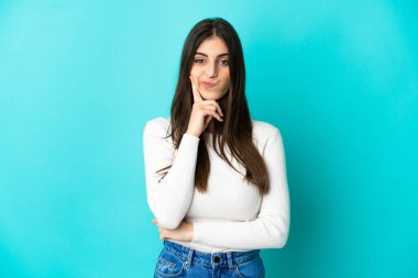 Kafkasyalı genç bir kadın mavi arka planda izole edilmiş ve düşünüyor