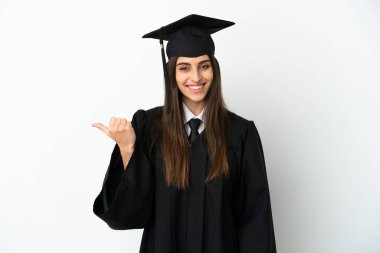 Beyaz arka planda izole edilmiş genç üniversite mezunu bir ürünü sunmak için kenarı işaret ediyor