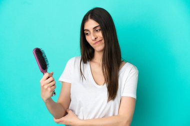 Young caucasian woman with hair comb isolated on blue background with sad expression