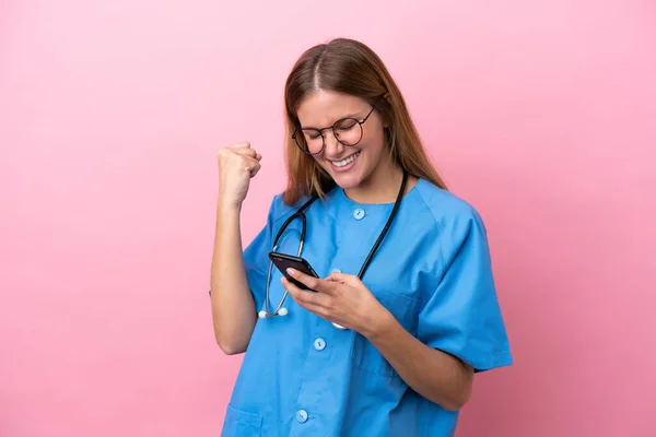 stock image Young surgeon doctor woman isolated on pink background with phone in victory position