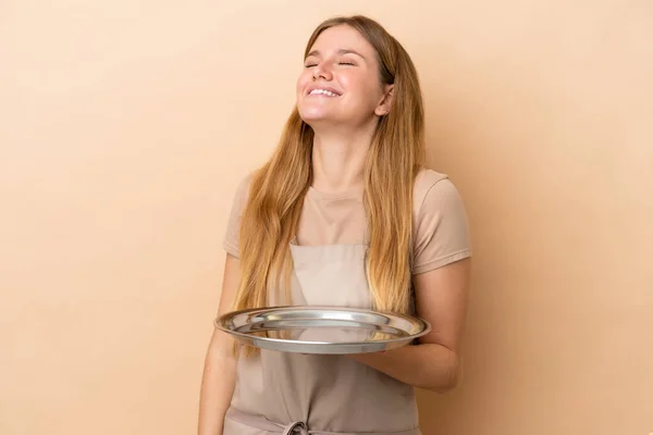 Młoda Blondynka Kelnerka Tacą Odizolowana Beżowym Tle Śmieje Się — Zdjęcie stockowe