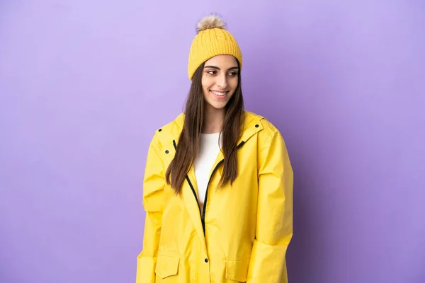 Νεαρή Καυκάσια Γυναίκα Φορώντας Αδιάβροχο Παλτό Απομονωμένο Μωβ Φόντο Αναζητούν — Φωτογραφία Αρχείου