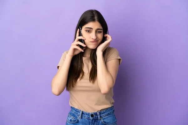 紫の背景に孤立した携帯電話を使用して若い白人女性フラストレーションとカバー耳 — ストック写真