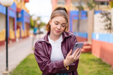 Dışarıda cep telefonu kullanan güzel bir kız. Üzgün bir ifadeyle.