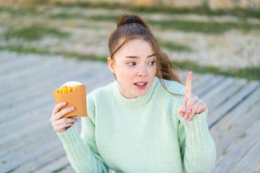 Dışarıda patates kızartması tutan genç ve güzel bir kız parmak kaldırarak çözümü bulmaya çalışıyor.