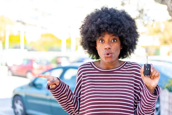 African American girl holding car keys at outdoors surprised and pointing side