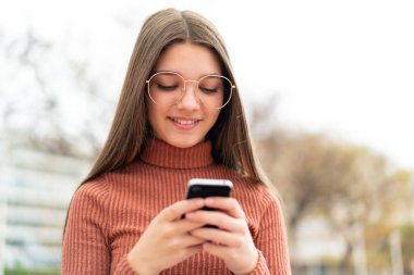 Dışarıdaki genç kız cep telefonuyla mesaj yolluyor.
