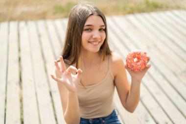 Genç kız açık havada donut tutuyor. Parmaklarıyla 