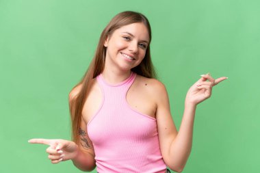 Genç, güzel, sarışın bir kadın izole edilmiş arka planda, parmak uçlarını işaret ediyor ve mutlu.