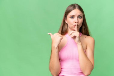 Genç, güzel, sarışın bir kadın, izole edilmiş arka planda. Yan tarafı işaret ediyor ve sessiz hareketler yapıyor.