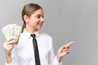 Young business caucasian woman holding money over isolated background pointing to the side to present a product