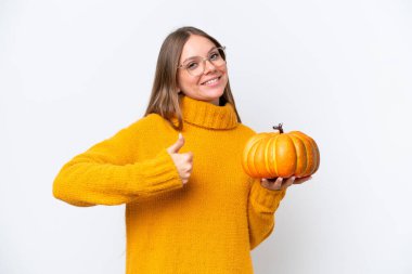 Young caucasian woman holding a pumpkin isolated on white background with thumbs up because something good has happened