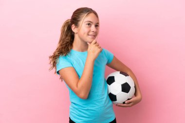 Little football player girl isolated on pink background looking to the side and smiling