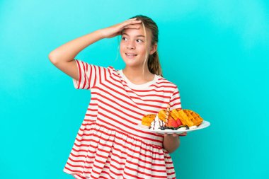 Mavi arka planda izole edilmiş waffleları tutan küçük beyaz kız çok gülümsüyor.