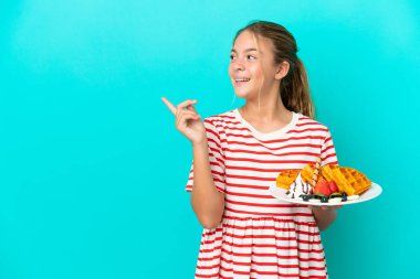 Mavi arka planda izole edilmiş waffle 'lar tutan küçük beyaz kız çözümü bulmak için parmağını kaldırıyor.