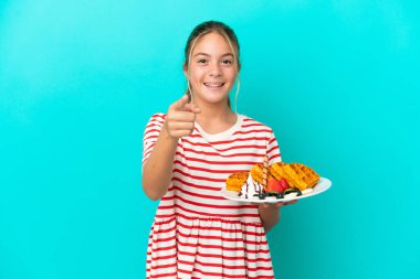 Mavi arka planda gözleme tutan küçük beyaz kız şaşırmış ve ön tarafı işaret ediyor.