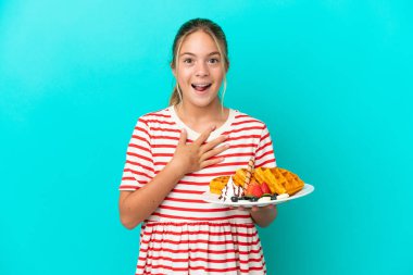 Mavi arka planda gözleme tutan küçük beyaz kız sağa bakarken şaşırdı ve şok oldu.