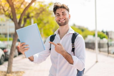 Genç yakışıklı bir öğrenci açık havada ve onu işaret ediyor.
