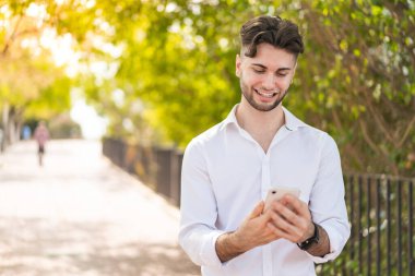 Dışarıdaki yakışıklı genç adam cep telefonuyla mesaj yolluyor.