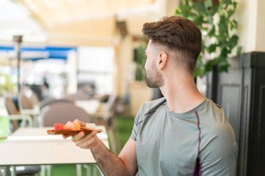 Genç yakışıklı adam arka tarafta saşimi tutuyor.